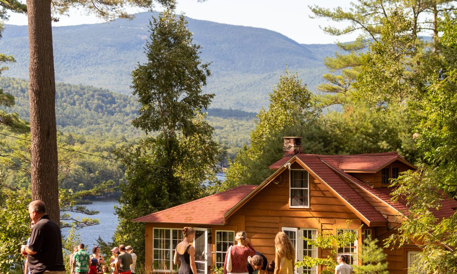 Exterior photo of a cabin and view to the lake with people gathered during a public event day