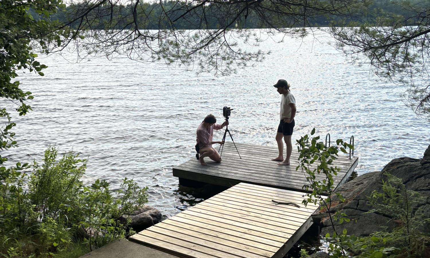 Two artists stand on the lakeside dock making a photo