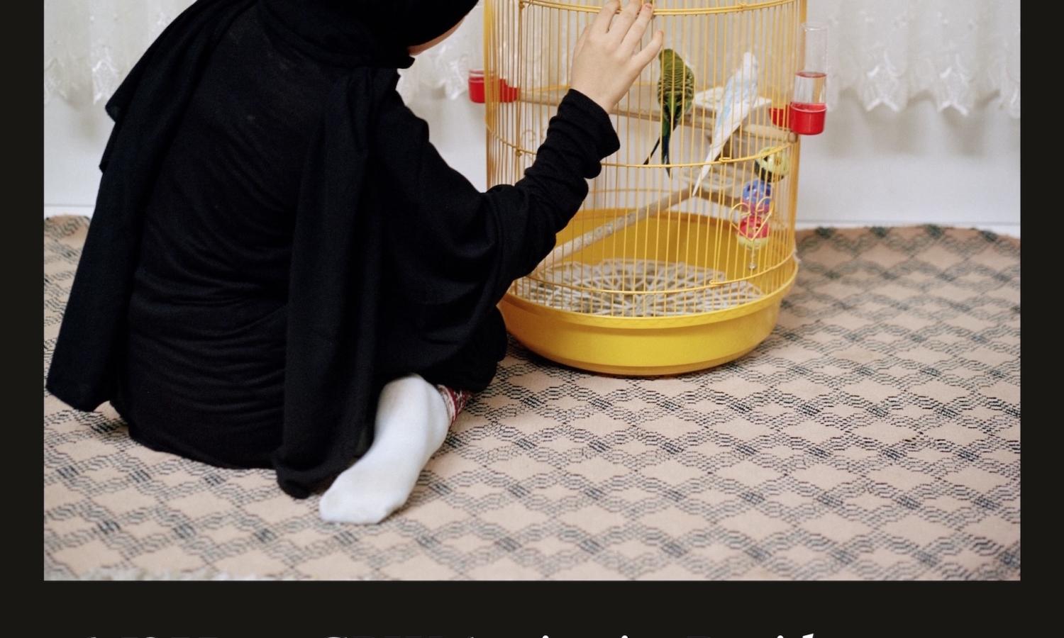 Girl kneels in front of yellow bird cage