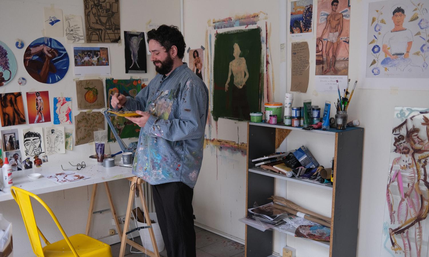 A painter in residence working in his studio, with paintings and inspirational images hung up on the walls
