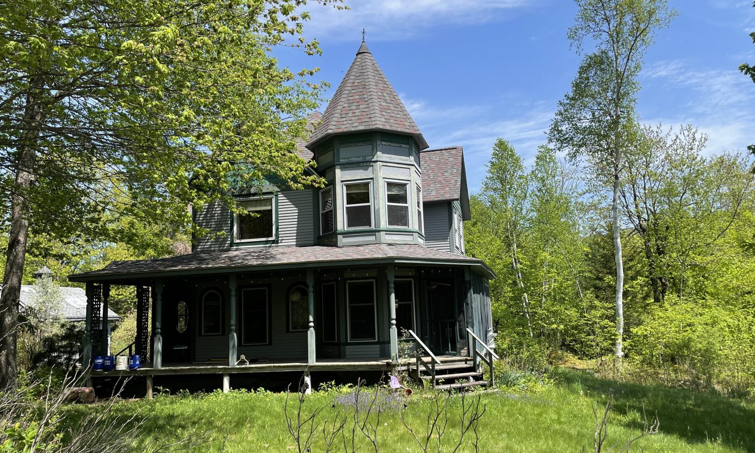 Kindred CRAFT Dream House, a victorian-style house surrounded by full, lush green trees.  Light blue sky.