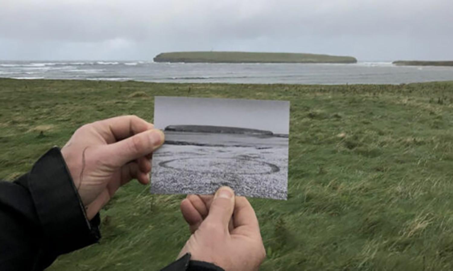 Hands hold a drawing in front of island vista