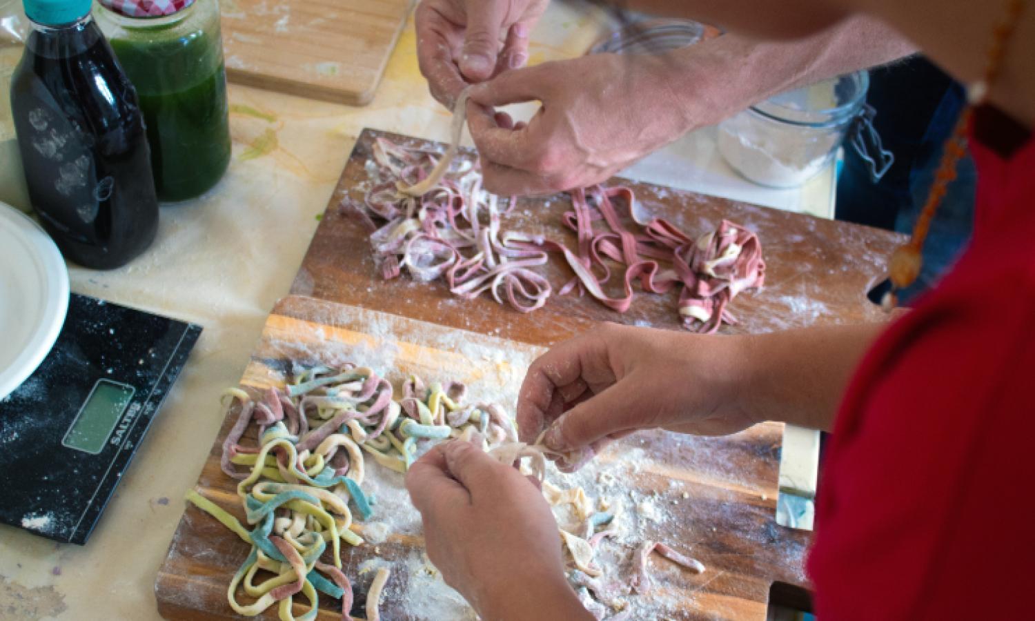 Close up of two pairs of hands working with raw pasta on a floured surface