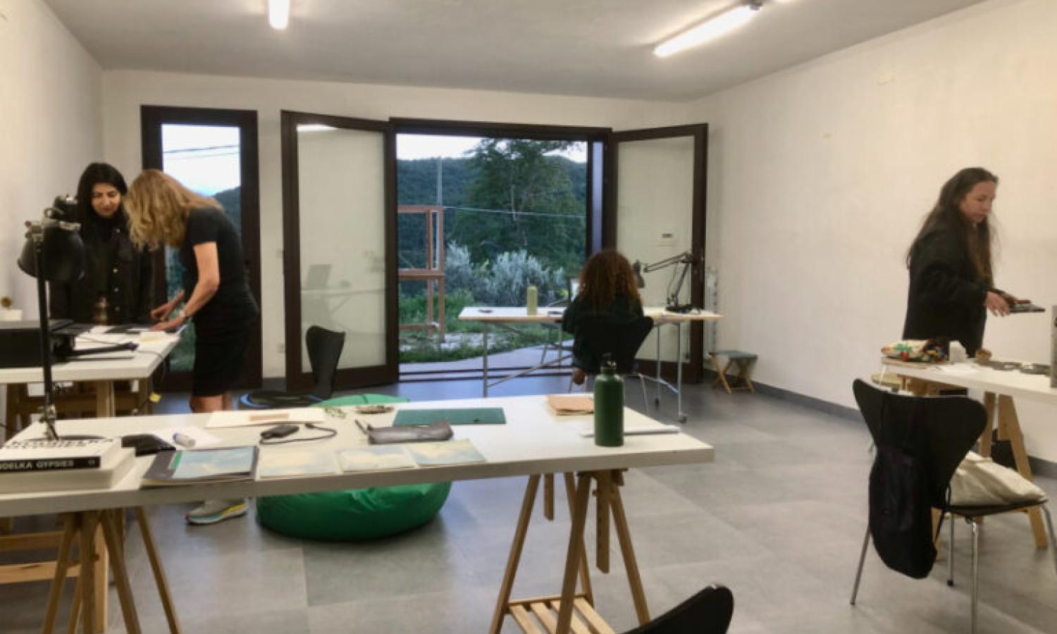 Four people workng in a white walled room with tressel tables and large french windows