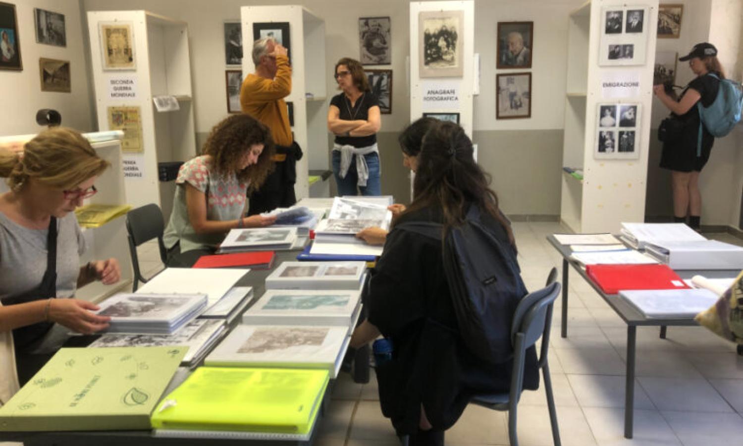 A group of people in a white walled room with tables and shelves displaying books and prints