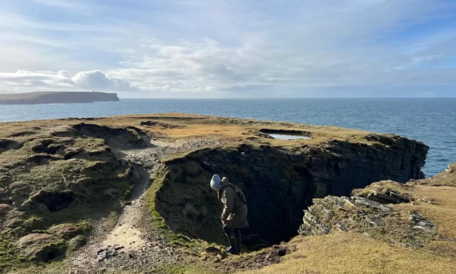 A figure on a rugged island headland with sea and sky beyond