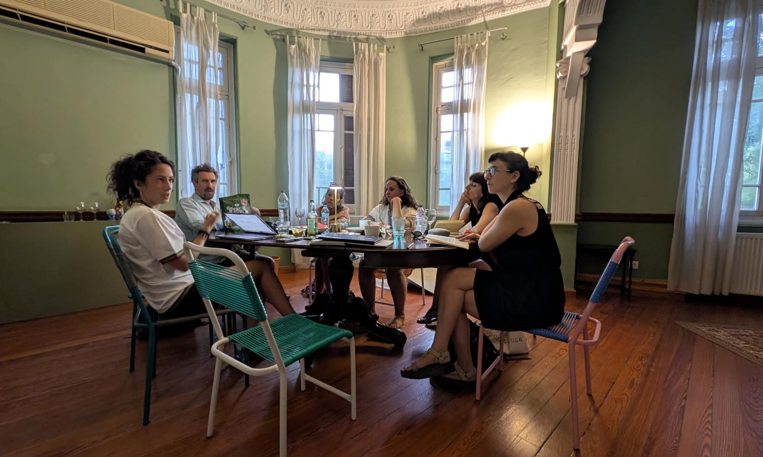 Residents gather in the Mansions for a collaborative devising session. Five individuals sit around a wooden table.