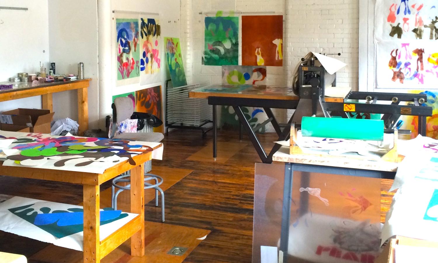 Image of the Private Residency Annex at Zea Mays Printmaking. Depicts a room with several work tables and colorful prints on the walls.