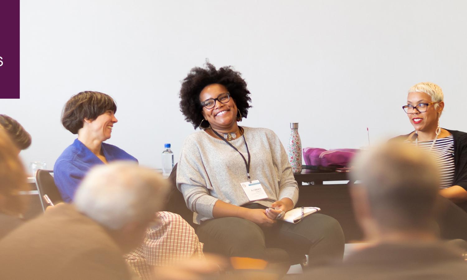 A group of panelists sit in front of an out-of-focus crowd.