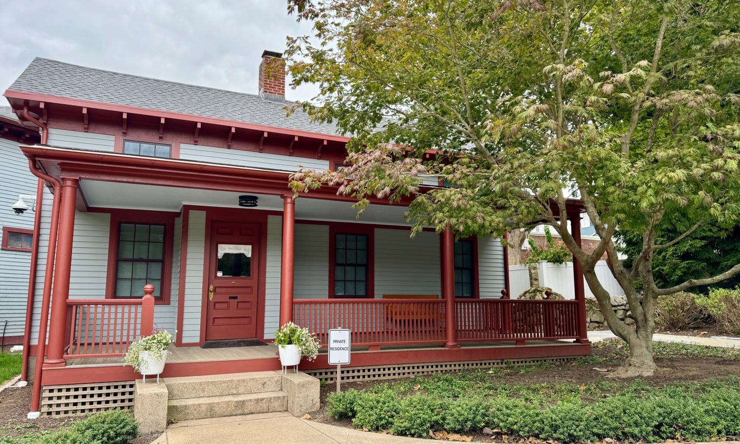 blue and burgundy cottage with porch in wilcox park with tree next to it.