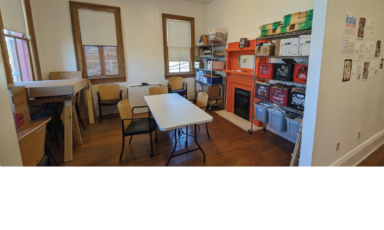 Kolaj Institute studio with work tables, collage supplies, shelving, and an orange fireplace used for material storage.