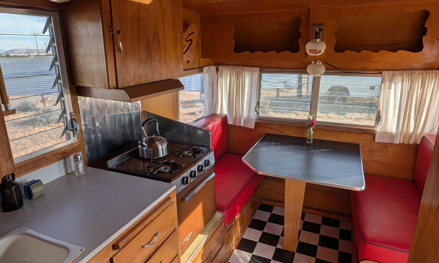 The interior of a vintage travel trailer, showing a small kitchen and seating area with table.