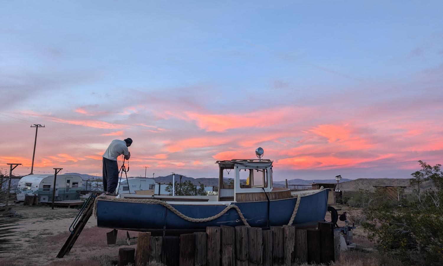 Person standing on top of a boat, taking a photograph of a sunset.