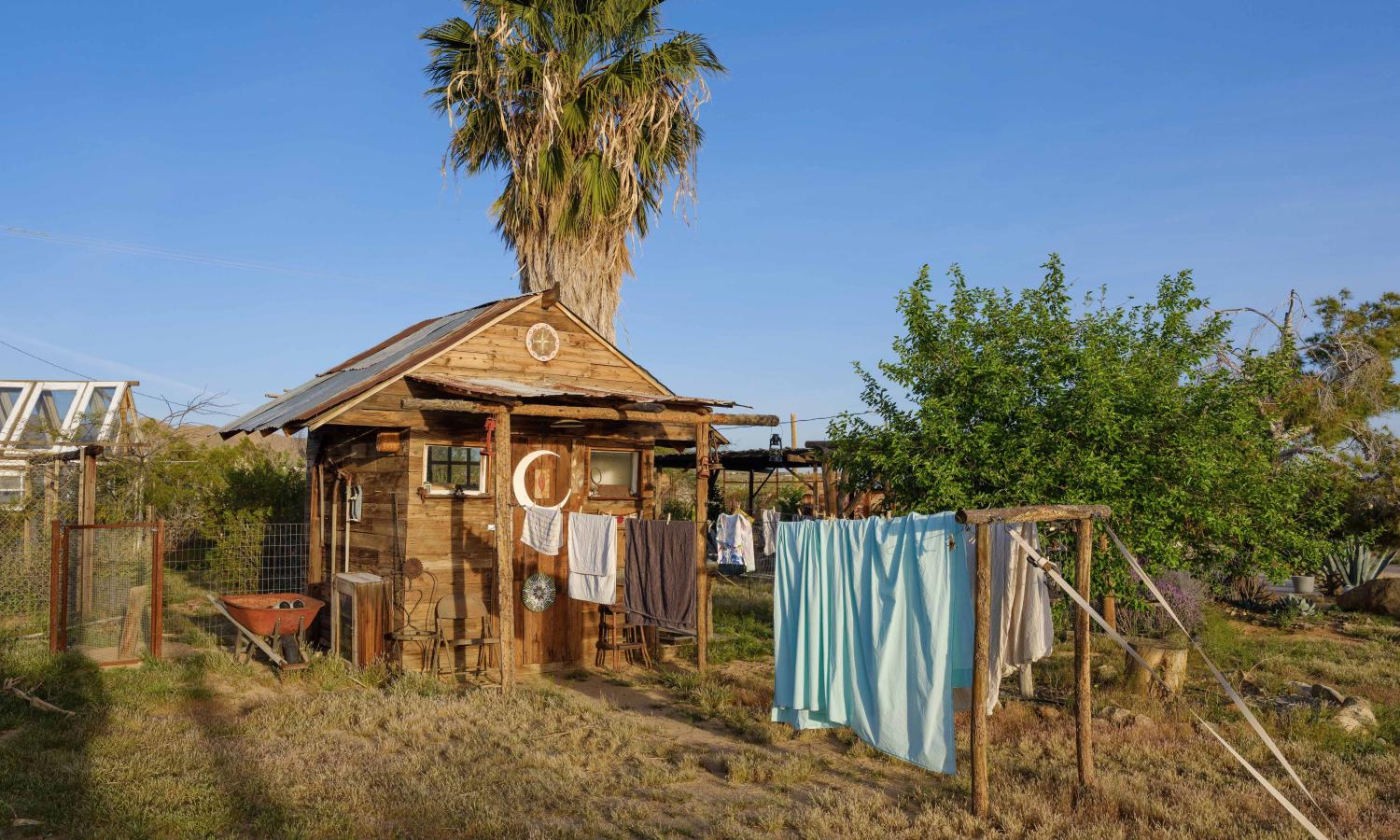 Small rustic wooden building with laundry hanging on a line, and palm tree in background.
