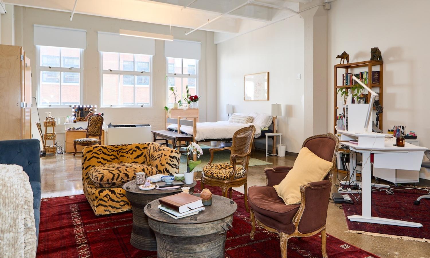 view of furnished live/work studio with wall of large windows in the background and visible bed as well as sitting area with chairs and a couch