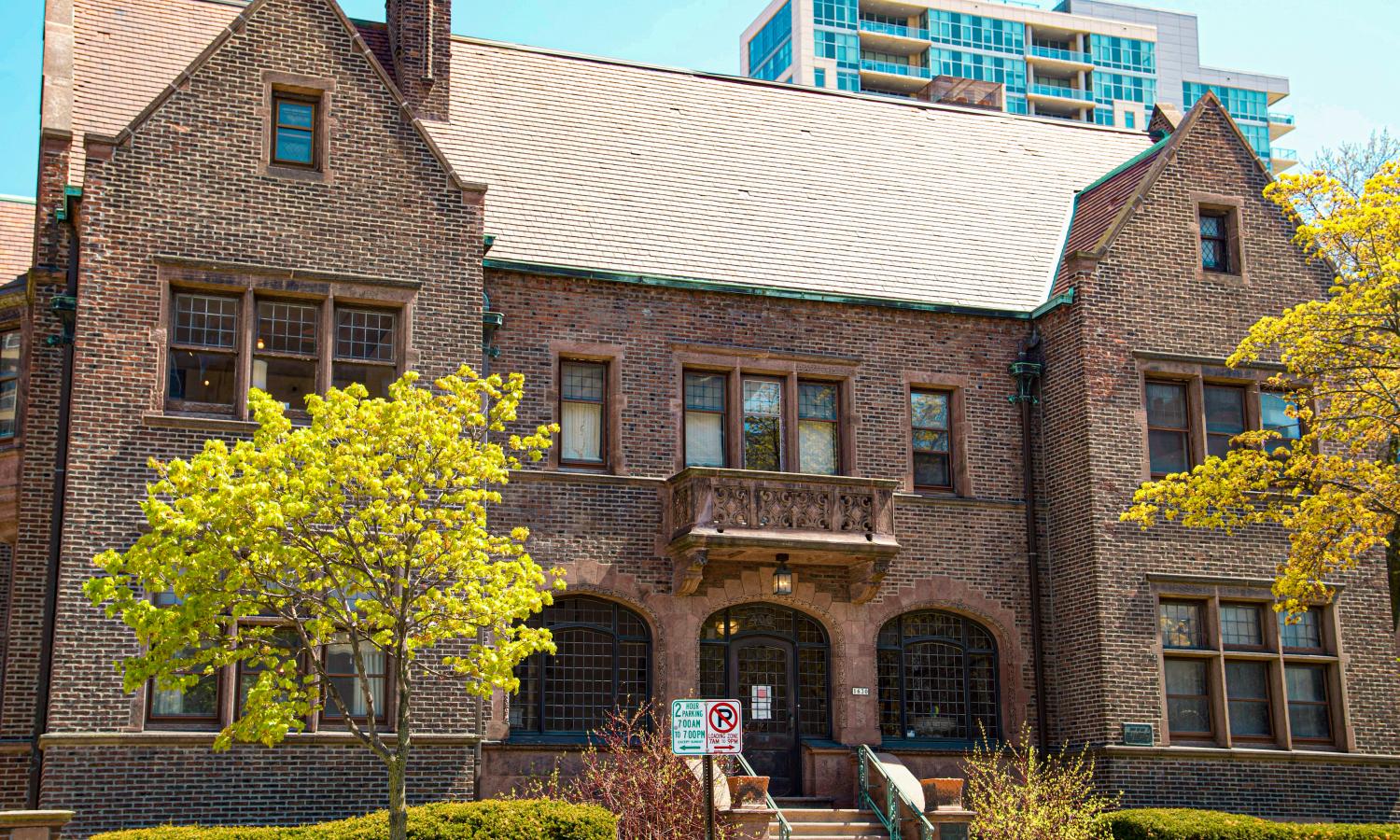 A tudor style brick building with a tree covering the left window.  A staircase goes up to a curved top door.  A small balcony is above that entry.