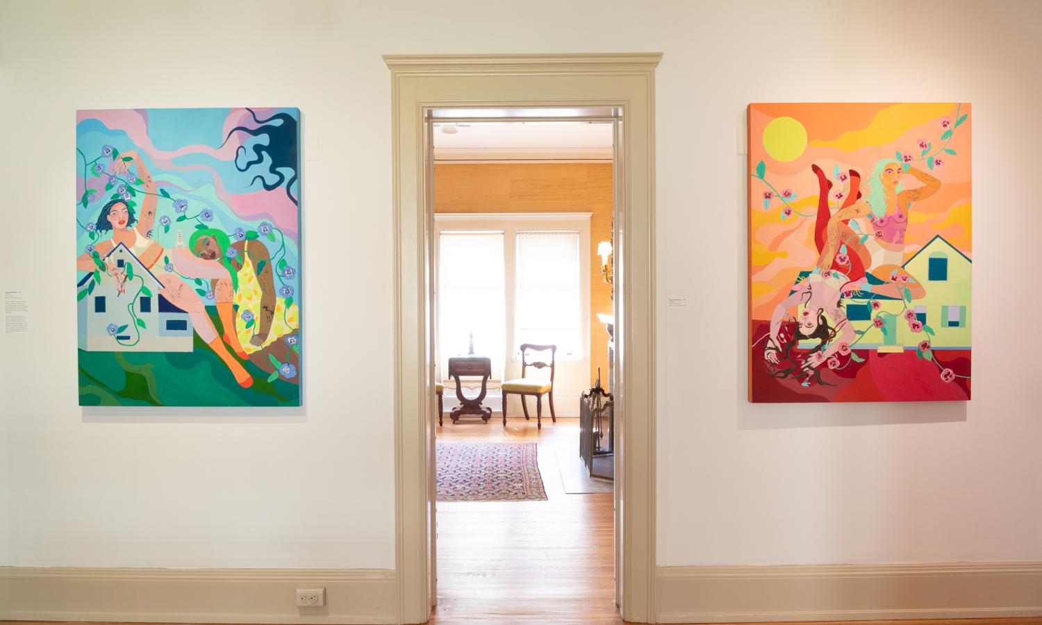 Looking into a room without a door flanked by two guache paintings on stretched canvas of a colorful fantasy style depiction.